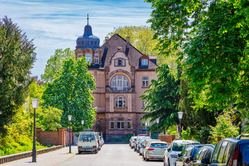 Historic building stands tall along a tree-lined street in a suburban area during a sunny day © Fleuronica