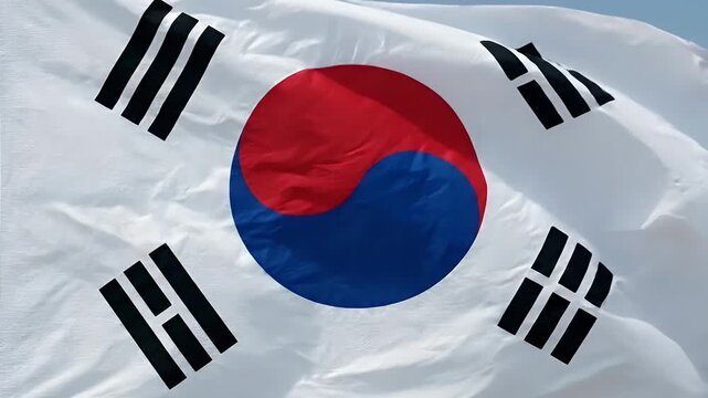 A close-up view of the South Korean flag, featuring its distinctive red and blue circle (taegeuk) and four black trigrams on a white field, fluttering gracefully in the wind.