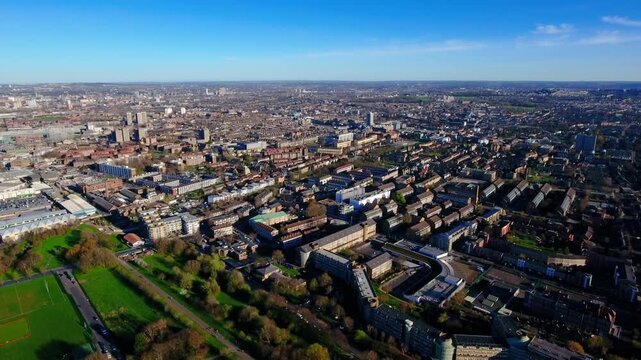 4K aerial view of Burgess Park with rugby pitch, Southwark housing estates, Aylesbury Estate, residential blocks and South London suburbs stretching to the horizon under blue sky.