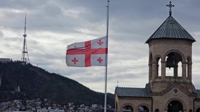 Flags wave at church tower in Tbilisi during cloudy weather in Georgia