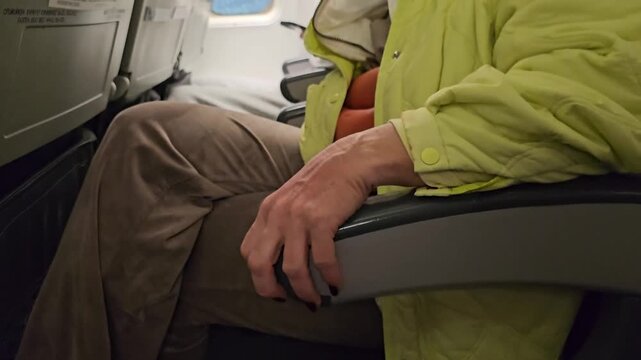 Passenger rests hand on armrest during flight in airplane seat in a busy cabin