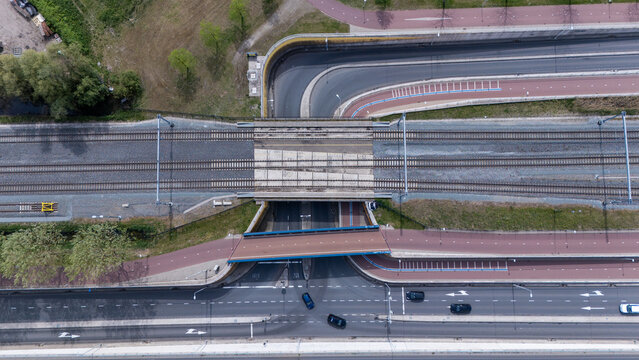 Top down aerial view of Dutch transport infrastructure with railway tracks, bicycle paths and car roads crossing each other. Urban mobility network showing different forms of transportation in holland