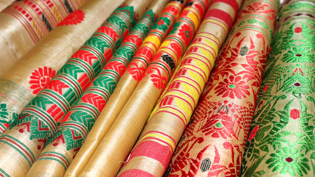 Traditional Assamese silk mekhela chador fabrics with colourful woven floral and geometric patterns displayed in a textile shop