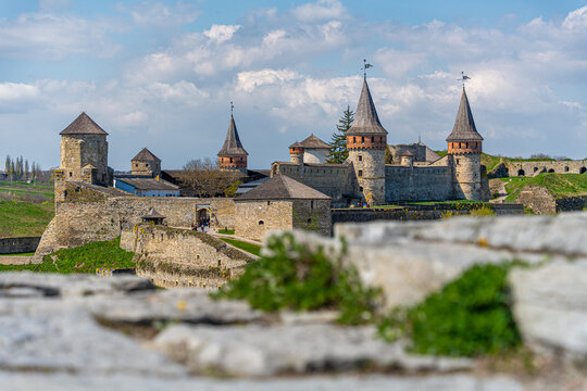 View of Kamianets-Podilskyi Castle with its medieval stone towers and fortified walls under a bright blue sky with fluffy white clouds Kamianets-Podilskyi, Khmelnytska oblast, Ukraine.