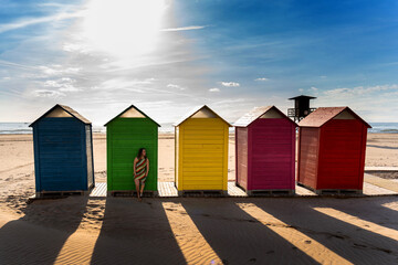Fototapeta premium Woman with a prosthetic leg posing by vibrant beach huts, feeling inclusive and free