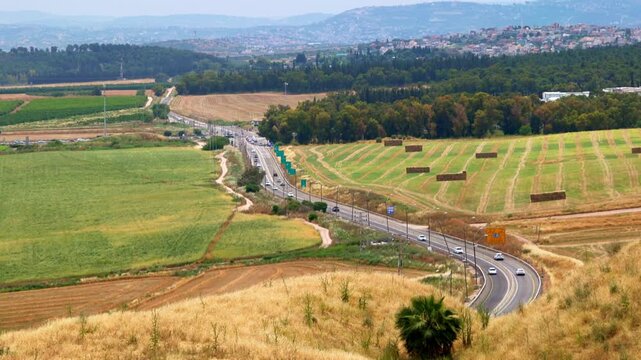 Israel, Megiddo, Daytime. High angle scenic view of a highway winding through lush agricultural fields and green hills of the Jezreel Valley in the northern district during a bright sunny day