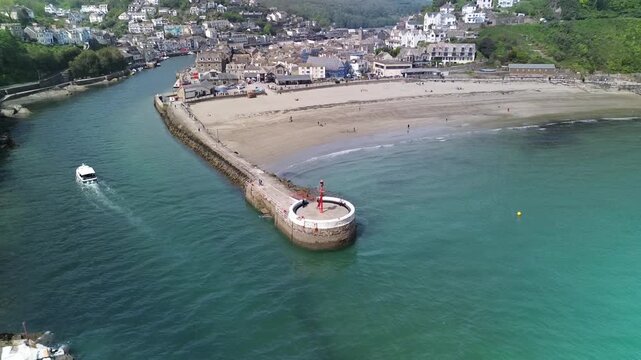 Cinematic 4K drone footage of Banjo Pier in Looe, Cornwall, filmed on a bright sunny day. A slow pull-back and rise reveals the wider harbour, town and a returning boat entering port.