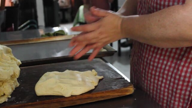 Hands of an unrecognizable woman are making achira biscuits with corn flour and placing them on a metal tray on a table inside her home in Yaguara, Huila, Colombia. Concept of handmade and raw food