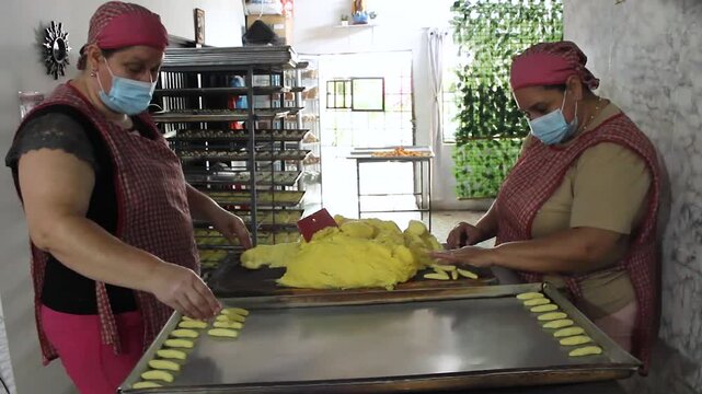 Two Colombian women wearing aprons are making achira biscuits with corn flour and then placing them on a table in a kitchen in Yaguara, Huila, Colombia. Concept of artisanal food and teamwork