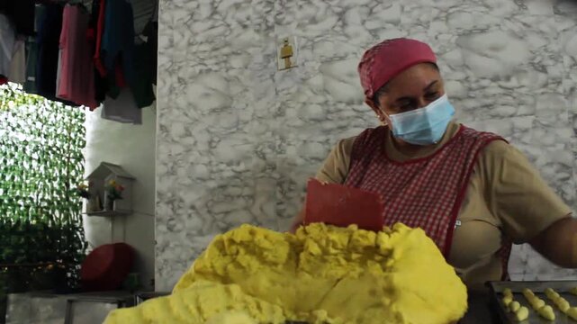 A Hispanic female chef is making achira biscuits with flour and then placing them on a metal tray on a table in a kitchen in Yaguara, Huila, Colombia. Concept of handmade and artisanal food