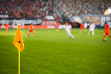Naklejka premium A close-up of a bright yellow corner flag on a grass pitch with a football match and stadium crowd blurred in the background.