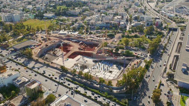 Expansive aerial footage showcasing a large construction site in a bustling city, highlighting the initial foundation and excavation phases amidst ongoing traffic on adjacent highways