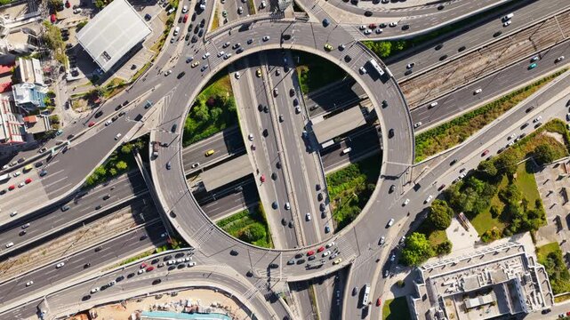 High altitude drone footage showing heavy vehicle traffic moving through a complex multi-level ring road and highway junction in a modern city, representing urban infrastructure