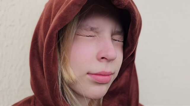 A teenage child in a hoodie looks down with tears and a serious expression. Loneliness, stress, depression, and resentment in a teenager