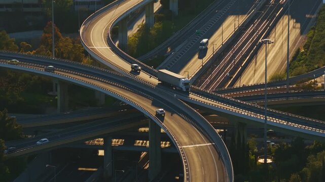 High-angle view of a bustling urban highway interchange with intricate ramps and overpasses, showing vehicles and trucks driving in multiple directions during a beautiful sunny day