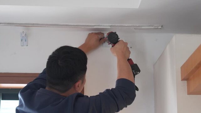 Man installing ceiling light fixture using cordless drill in modern home interior