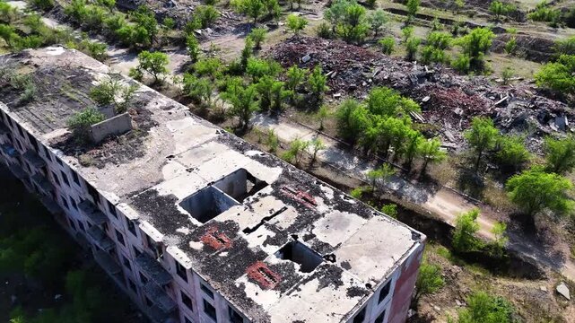 Drone orbit around an abandoned Soviet panel apartment building with a collapsed roof in Chagan ghost town. A former secret military site in Kazakhstan. Footage highlights architectural 