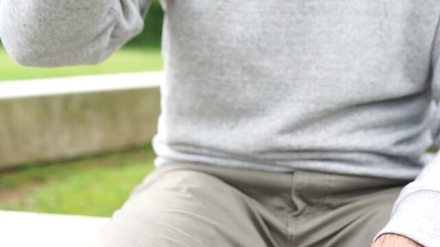 Close-up of a man opening and drinking from a PET plastic water bottle while sitting in a park, illustrating plastic consumption.