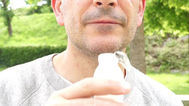 Close-up of a man drinking a dairy product from a small plastic bottle, showing the use of synthetic materials in food packaging.