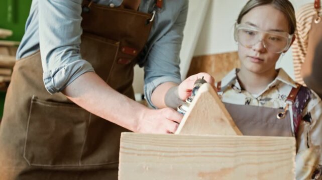 Rack focus shot of unrecognisable woodworking instructor lighting propane torch and burning wooden piece while teaching teenage girl in workshop