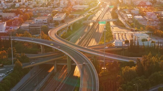 Golden hour sunlight illuminating a multi-level highway interchange with cars and trucks driving through the complex road network, showing urban infrastructure and transportation concepts