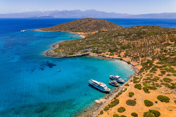 Fototapeta premium Drone shot of tourist boats anchored in a crystal clear blue bay in Crete, Greece