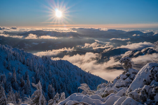 View of Salatin mountain peak with a bright sunburst over mist-filled valleys and snow-covered pine trees in Liptovska Stiavnica, Zilinsky kraj, Slovakia.