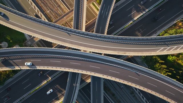 Majestic aerial top-down view of a complex highway interchange with multiple overpasses and ramps, showing cars and trucks driving along the intricate road network surrounded by greenery