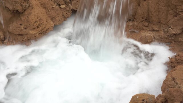 Close-up tilt-down shot of a high-volume stream of water pumping from a rusty industrial pipe into a foamy dirt basin. Ideal dynamic B-roll for dewatering, irrigation, and groundwater extraction.