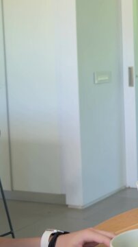 Vertical video: Reaching youth in rust tee with white watch passing bowl in kitchen, serving salad