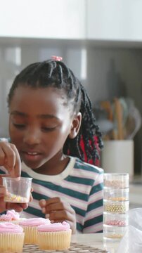 Vertical video: Holding sprinkles cup, nana guiding youth in stripes at home decorating cupcakes