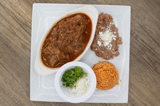 Overhead view of hearty plate of birria smothered in consome, beans, and rice to satisfy that urge for a Mexican food meal