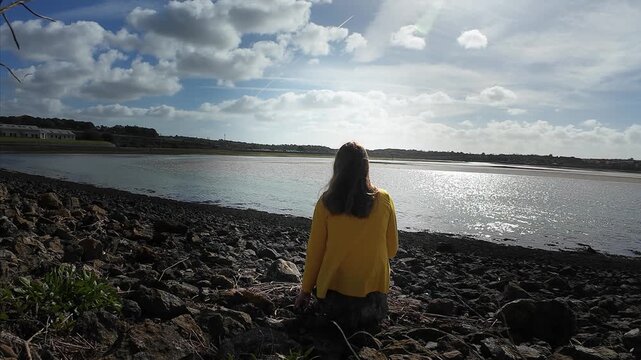 A woman walks on the evening seaside wearing yellow jacket