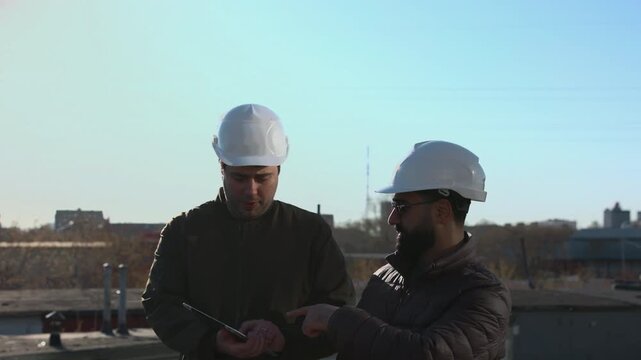 Two Technicians On Rooftop Planning Drone Flight Path While Checking Tablet Coordinates And Mapping Data. Media
