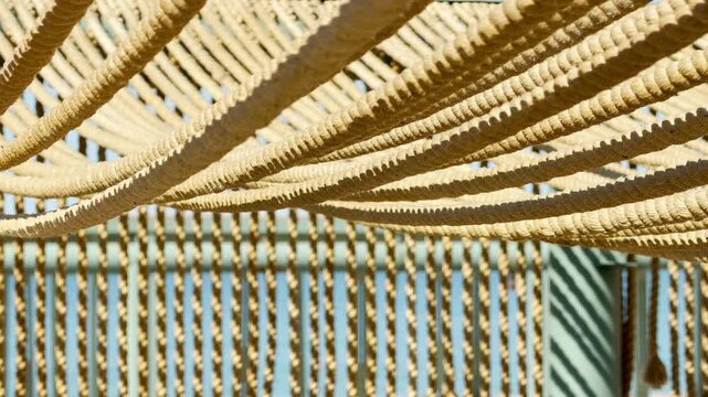 Thick, rustic ropes curve elegantly to create a layered canopy against the sunny sky. This warm, textured design offers a peaceful and cozy sense of shelter from the bright afternoon sun.