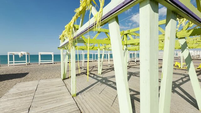 Pale green cabanas and weathered wooden walkways sit quietly along the empty coastline. The tattered yellow fabric creates a bittersweet yet peaceful feeling of calm summer days gone by.