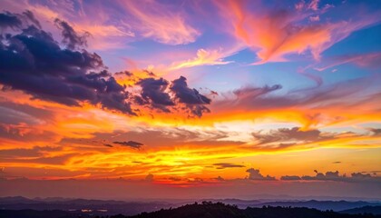 Fototapeta premium A vibrant sunset paints the sky with fiery hues over a rolling landscape, creating a breathtaking panorama of color and light.
