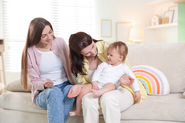 Obraz premium LGBT parents. Happy lesbian couple with their cute baby on sofa at home