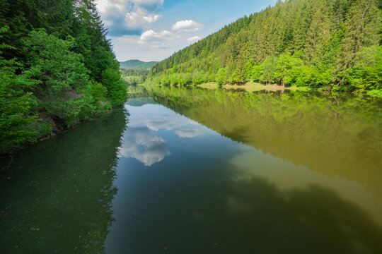 View of Vodna nadrz Hnusno reservoir reflecting the surrounding lush green forest and blue sky with clouds Horna Lehota, Banskobystricky kraj, Slovakia.