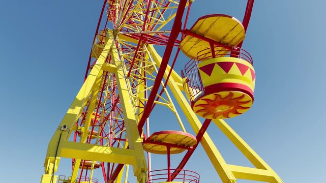 A bright yellow and red Ferris wheel stands tall on a perfectly clear day. This cheerful scene evokes feelings of carefree happiness, childlike wonder, and the thrill of summer carnivals.