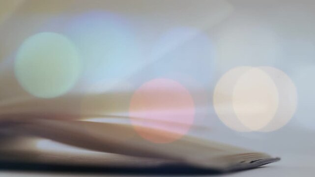 Left-edge lift starting thin stack pages lifting and fanning right over soft bokeh, forming wave