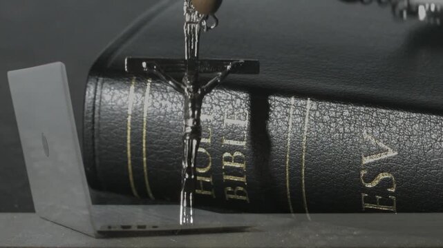 Metal crucifix pendant triggered by top entry, descending and swinging, settling across Holy Bible
