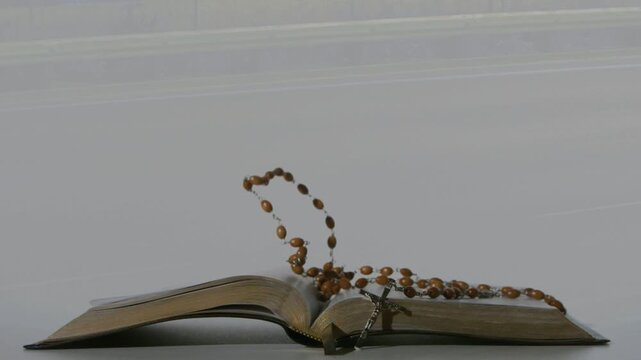 Subtle release sending rosary swinging onto open book, beads bouncing then settling to rest draped