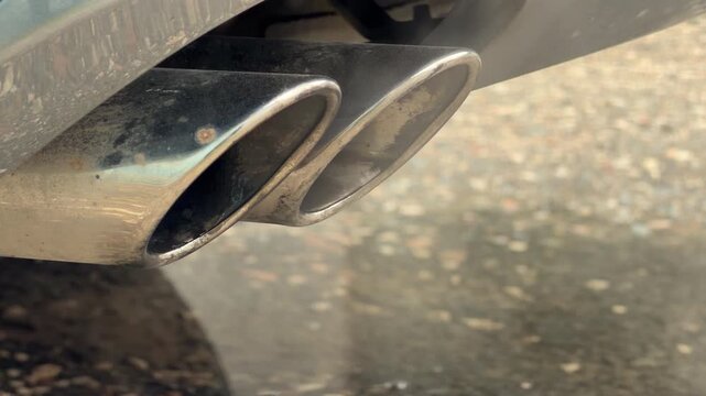 Warm exhaust fumes drift silently from the dual chrome tailpipes of a car. The damp and gloomy atmosphere of the wet ground reflects a cold, dreary morning in the city.