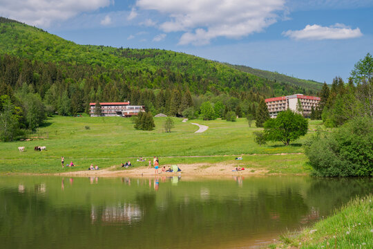 View of Krpacovo lake with people relaxing on the shore surrounded by lush green hills and hotels in Dolna Lehota, Banskobystricky kraj, Slovakia.