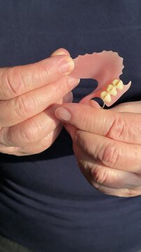 Close-up woman hands holding denture showcasing high-quality partial prosthesis patient inspecting fit and tooth detail against dark