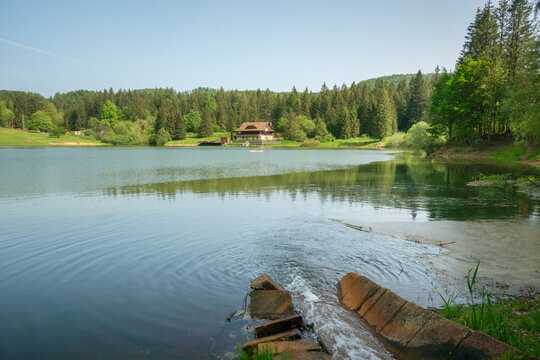 View of Krpacovo reservoir with a wooden chalet on the shore surrounded by a dense pine forest and calm water reflections in Dolna Lehota, Banskobystricky kraj, Slovakia.