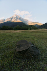 Naklejka premium A lone backpack sits on a grassy meadow with towering mountains in the background, capturing a moment of outdoor exploration and quiet solitude.