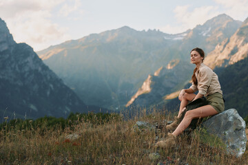 Naklejka premium Woman sits on a rock in a mountain meadow, enjoying the view. Outdoor lifestyle scene highlighting nature, solitude, and calm.
