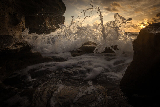 View of ocean waves crashing against dark rocks with sea foam and golden sunset light in Florida, United States.
